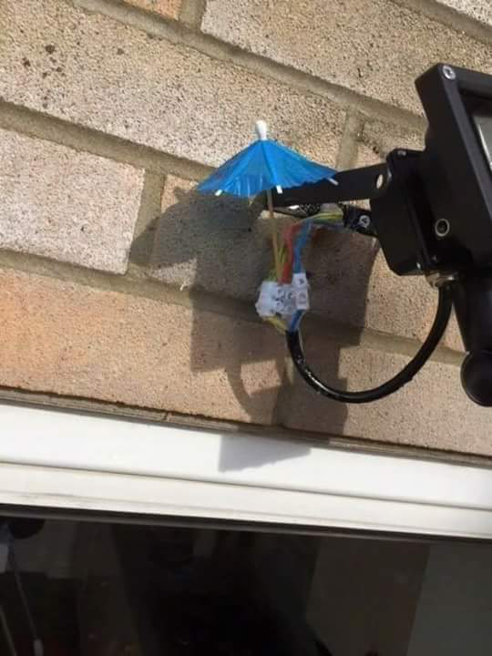 Een kleine papieren paraplu bedekt nauwelijks een open kroonsteen met electriciteitsdraden. Het vormt een hopeloos schild tegen regen.